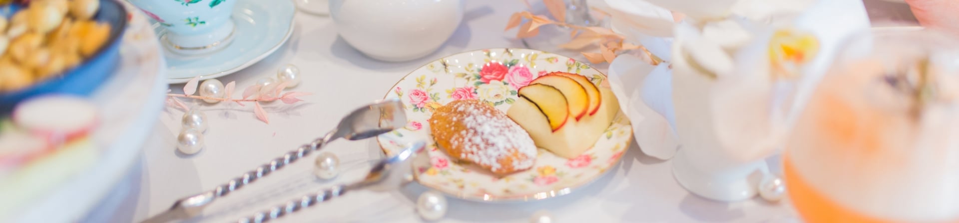 Cake bites, snacks, mixed drinks and tea cups laid on a table.