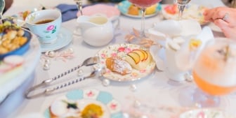 Cake bites, snacks, mixed drinks and tea cups laid on a table.