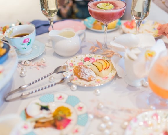 Cake bites, snacks, mixed drinks and tea cups laid on a table.