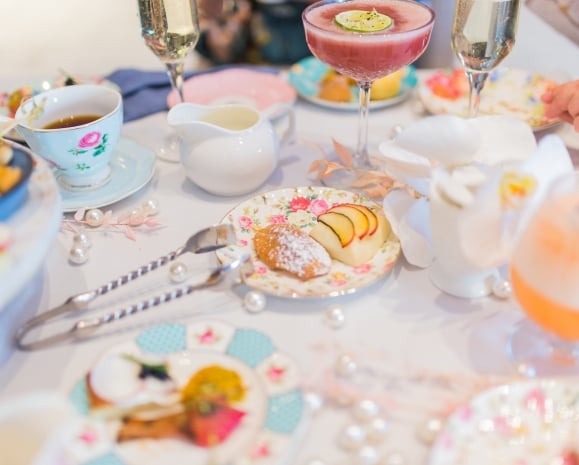 Cake bites, snacks, mixed drinks and tea cups laid on a table.