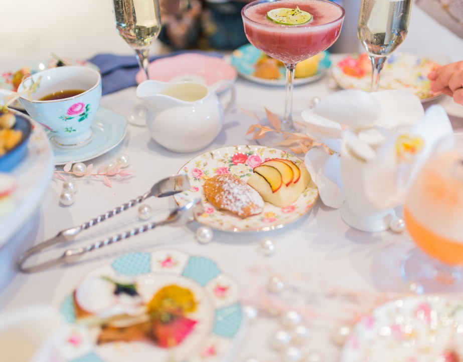 Cake bites, snacks, mixed drinks and tea cups laid on a table.