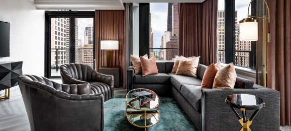 A sectional couch and two leather chairs in a hotel room.