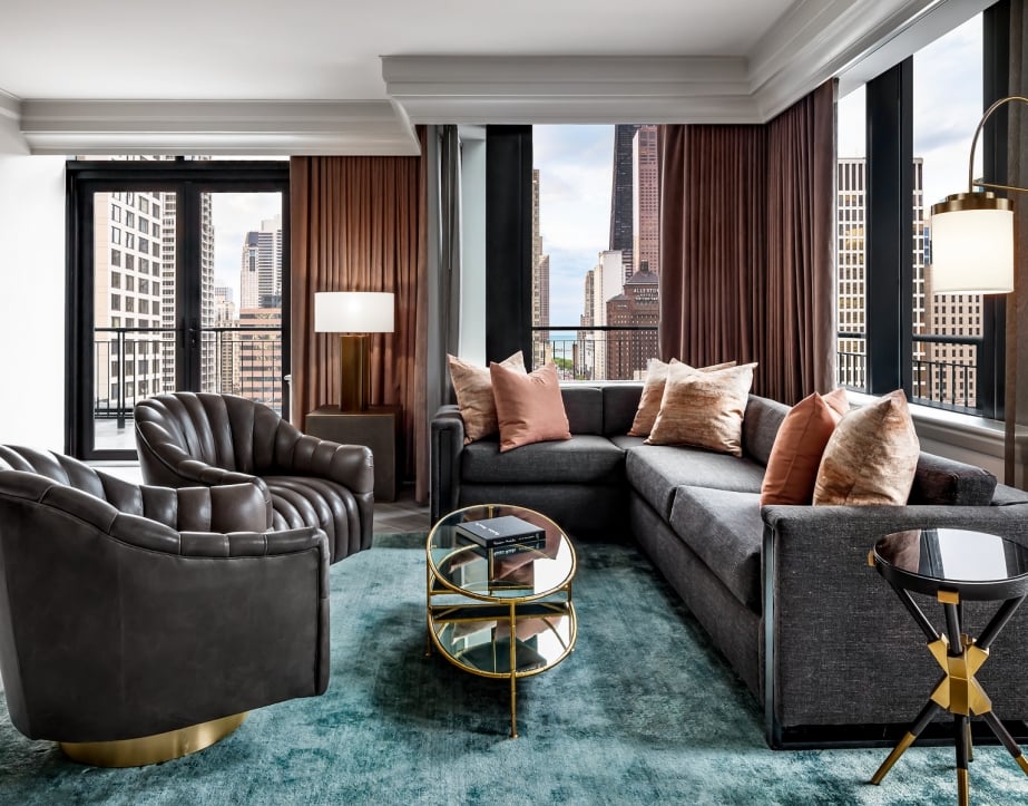 A sectional couch and two leather chairs in a hotel room.
