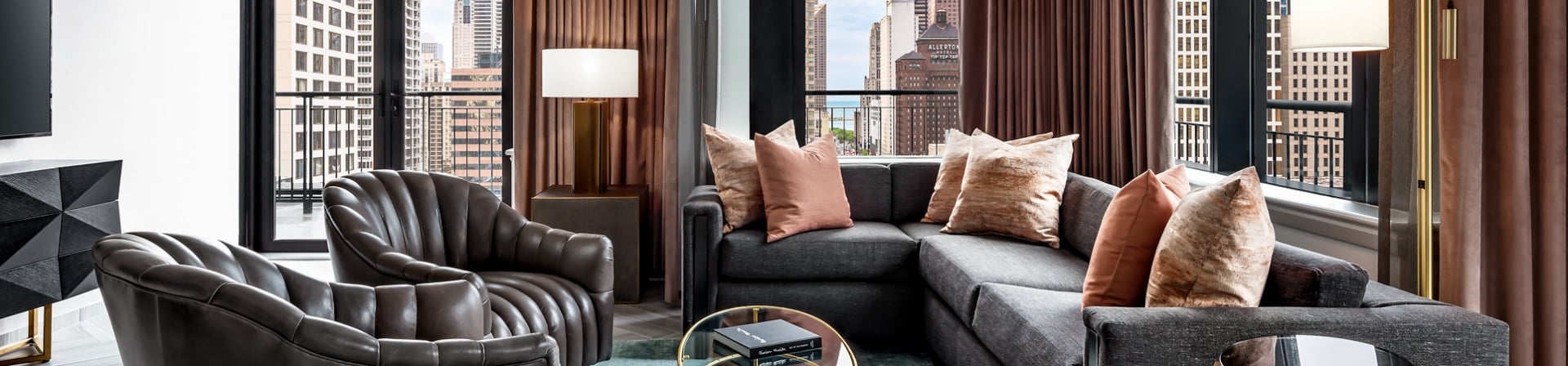 A brightly lit lounge area with a green rug and large sectional in the Gwen Lux Suite.