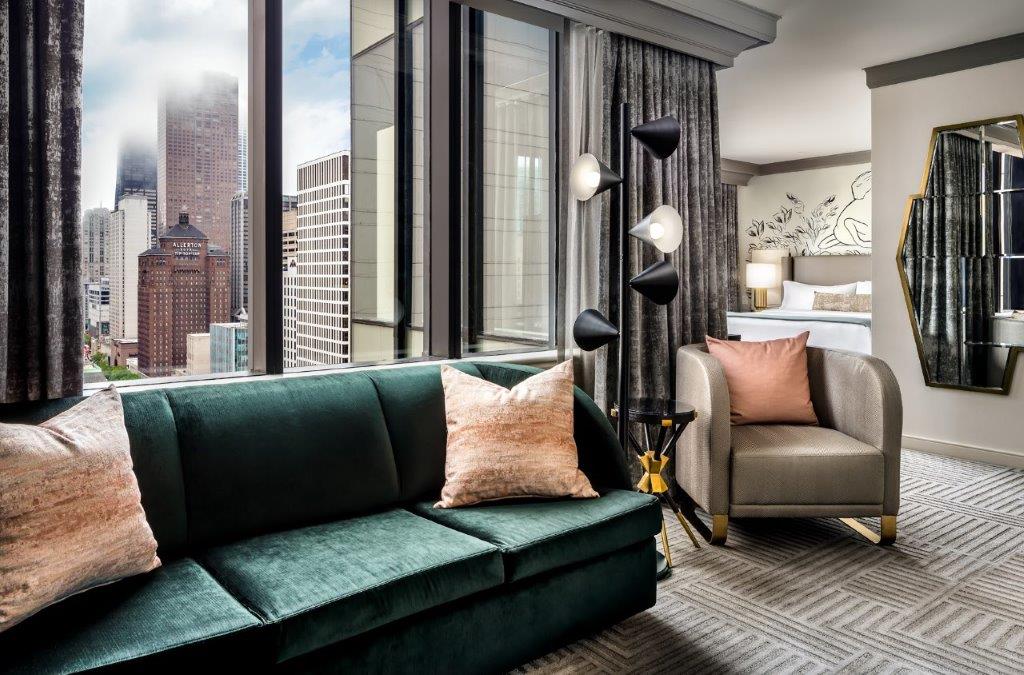 A green plush couch in front of large windows that show off downtown Chicago's buildings.