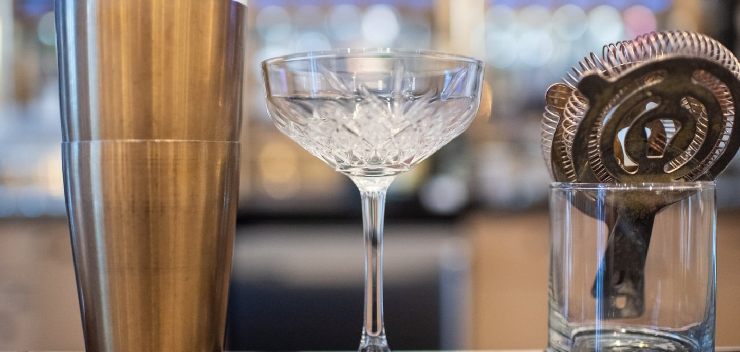 A shaker, cocktail glass and a rocks glass on a bar countertop.