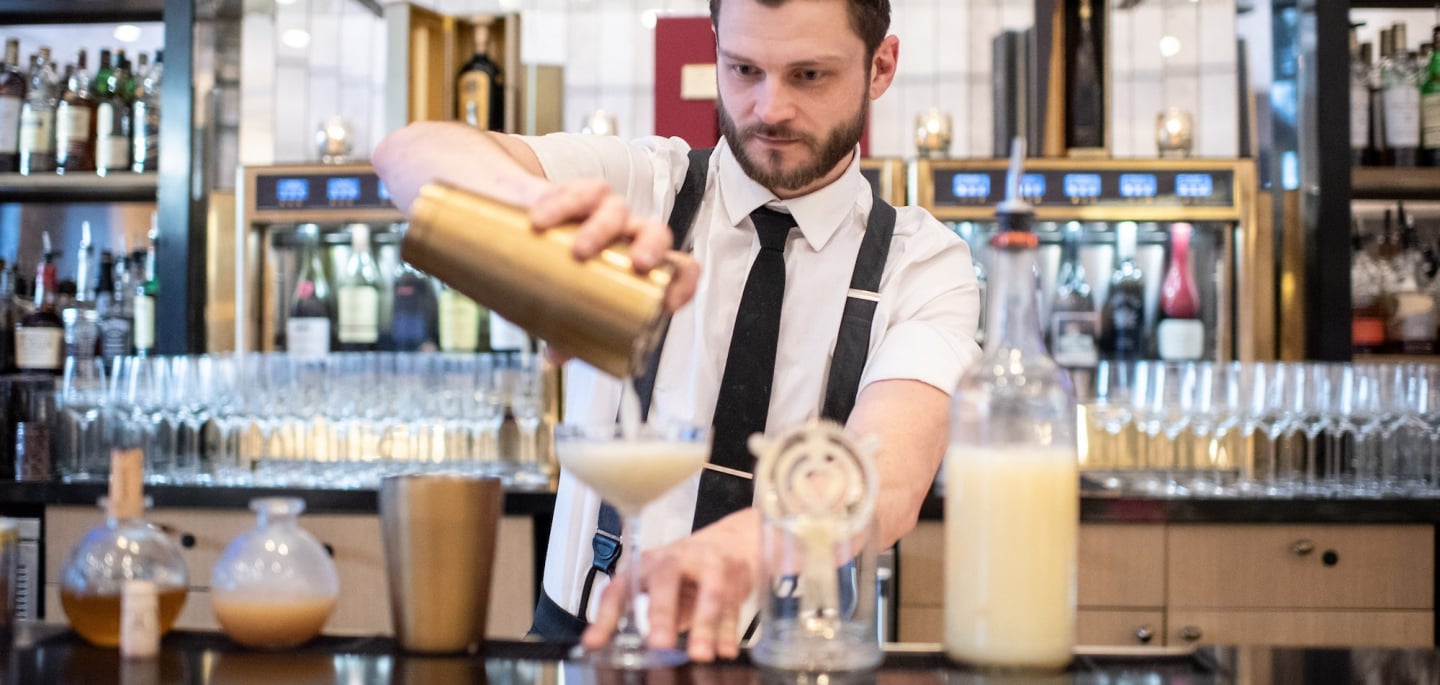 A bartender at Upstairs at The Gwen strains a drink into a cocktail glass.