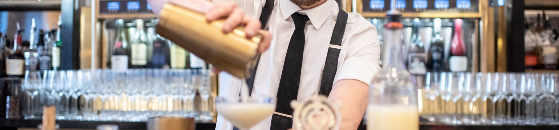A bartender at Upstairs at The Gwen strains a drink into a cocktail glass.
