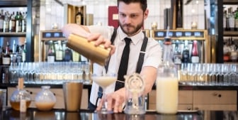 A bartender at Upstairs at The Gwen strains a drink into a cocktail glass.