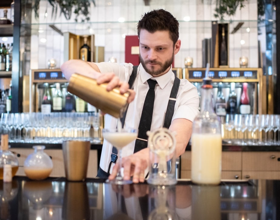 A bartender at Upstairs at The Gwen strains a drink into a cocktail glass.