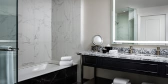 A bathroom with a full bath, large mirror and a marble countertop.