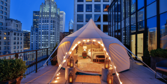 Tent with a bedroom set up on a downtown Chicago balcony with a cityscape in the background at nighttime