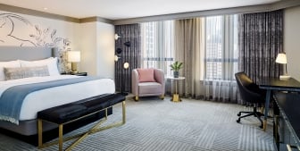 A hotel room with a large bed, small red chair and a work station.