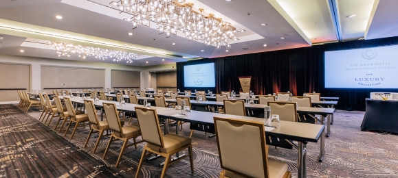 A large conference room with rows of tables, chairs and a large projector screen.