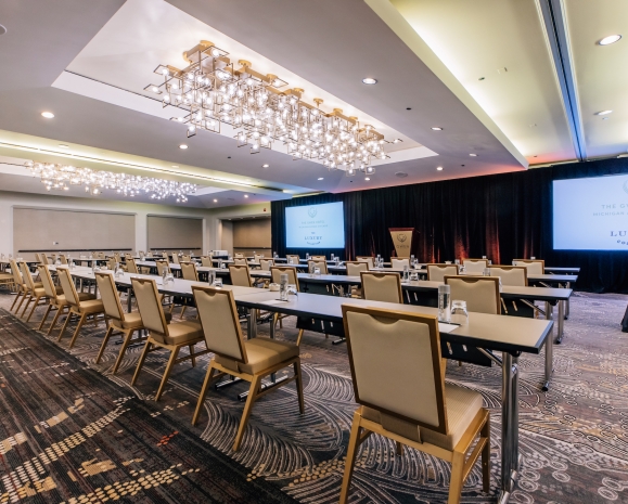 A large conference room with rows of tables, chairs and a large projector screen.