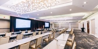 A large conference room with rows of tables, chairs and a large projector screen.