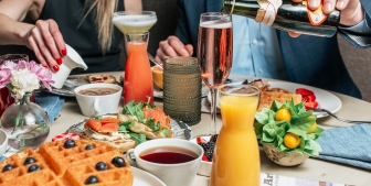 A table filled with brunch foods such as waffles, strawberries, orange juice and sparkling wine.