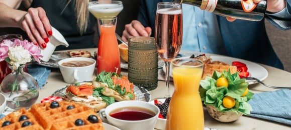 A table filled with brunch foods such as waffles, strawberries, orange juice and sparkling wine.