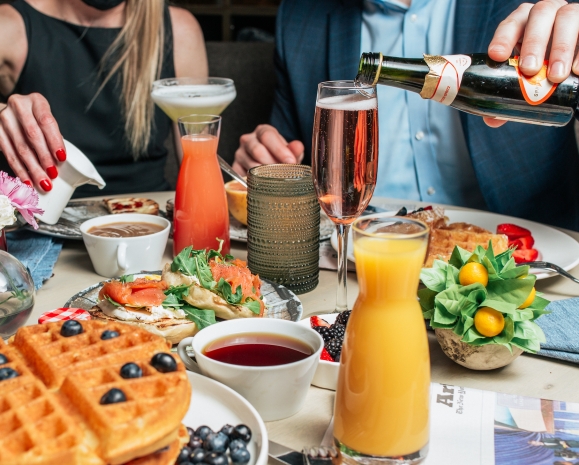 A table filled with brunch foods such as waffles, strawberries, orange juice and sparkling wine.