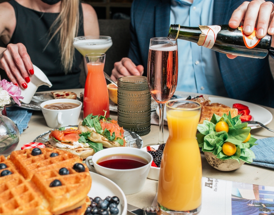 A table filled with brunch foods such as waffles, strawberries, orange juice and sparkling wine.