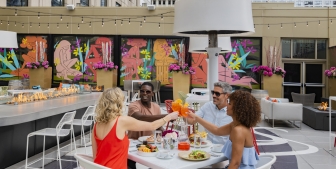 A group of friends smiling and 'cheersing' their drinks on the Upstairs at The Gwen's rooftop patio.