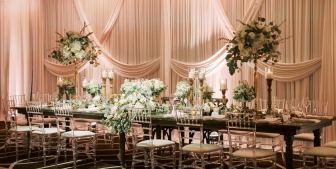 A beautifully designed head table at a wedding equipped with large candles, green bouquets and stylish décor.