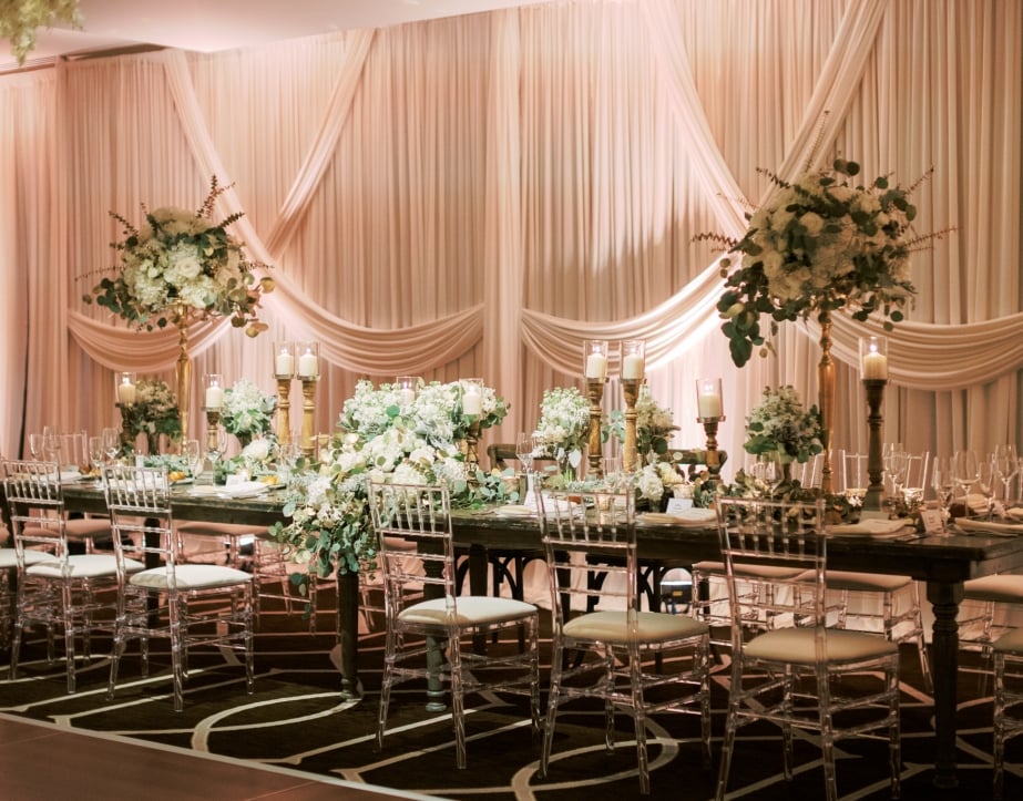 A beautifully designed head table at a wedding equipped with large candles, green bouquets and stylish décor.