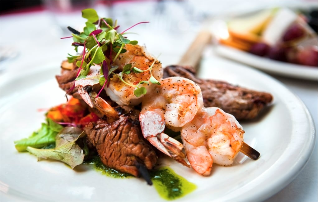 Shrimp and steak served with green garnishes on a white plate.