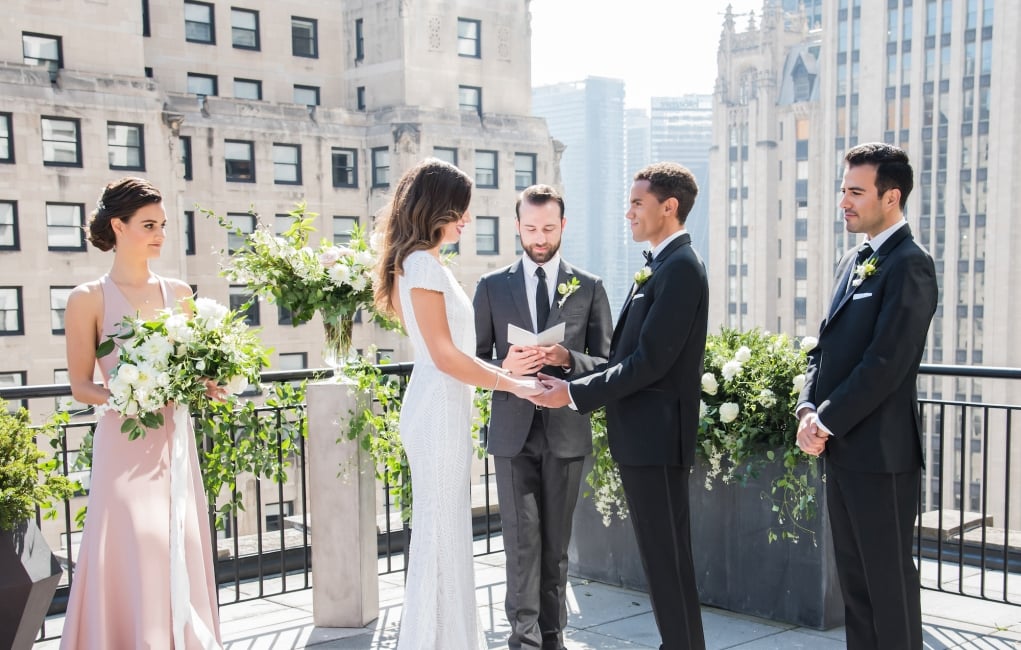 A bride and groom say their vows during their outdoor wedding on the sunny rooftop patio at The Gwen.