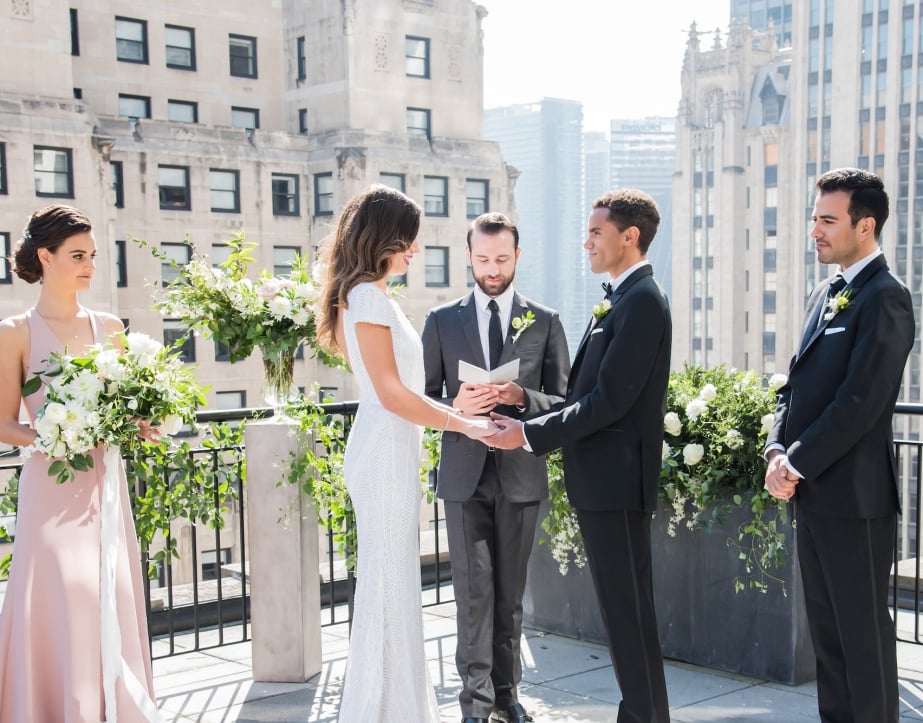 A bride and groom say their vows during their outdoor wedding on the sunny rooftop patio at The Gwen.